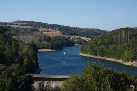Im Tal liegt zwischen Wäldern ein großer, blauer See hinter einer großen Mauer