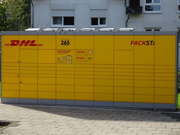 Eine gelbe DHL-Packstation steht vor einem Haus.