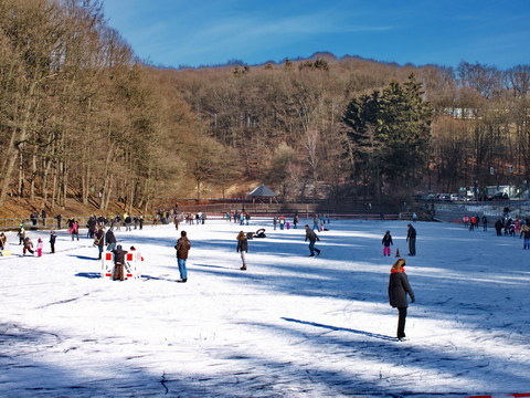 Menschen in bunten Jacken laufen auf dem gefrorenen Uelfebad Schlittschuh