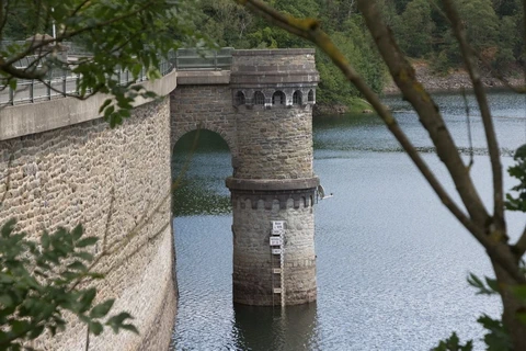 Neben der Staumauer steht ein Turm mit einer Pegeltafel daran im angestauten Wasser