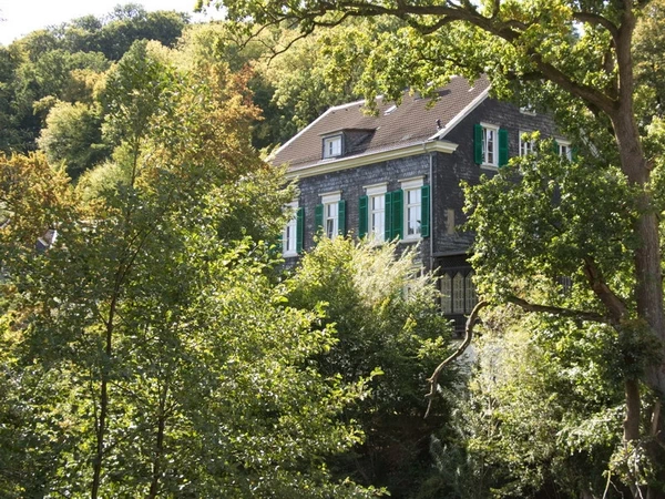 Typisch bergisches Schieferhaus mit grünen Schlagläden zwischen grünen Bäumen