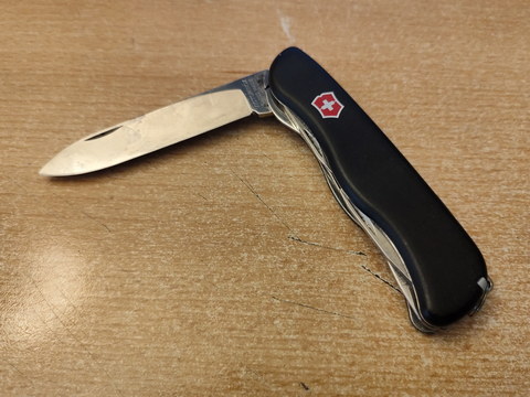 Auf einem Tisch liegt ein schwarzes, halb aufgeklapptes, Schweizer Taschenmesser