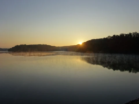 Über der stillen Wasserfläche der Bevertalsperre geht die Sonne auf
