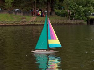 Ein Modellsegelboot mit grünem Großsegel und buntem Vorsegel segelt auf dem Uelfebad