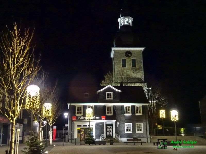 Radevormwalder Marktplatz bei Nacht. An den Laternen hängt Weihnachtsbeleuchtung und der Kirchturm im Hintergrund wird hell angestrahlt