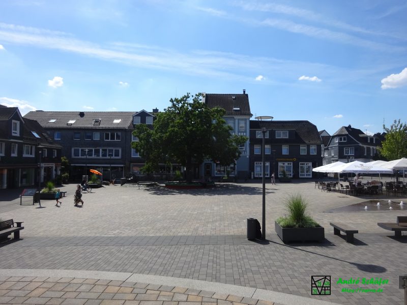 Blick über den neu, hellgrau gepflasterten Marktplatz Radevormwalds westwärts, wo die "Gründereiche" auf dem Platz in vollem Grün steht