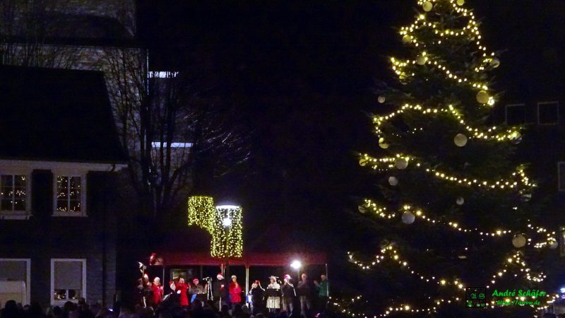 Vor der Kirche ist auf dem Marktplatz zum Weihnachtssingen eine kleine Bühne aufgebaut, auf der ein Chor Weihnachtslieder singt