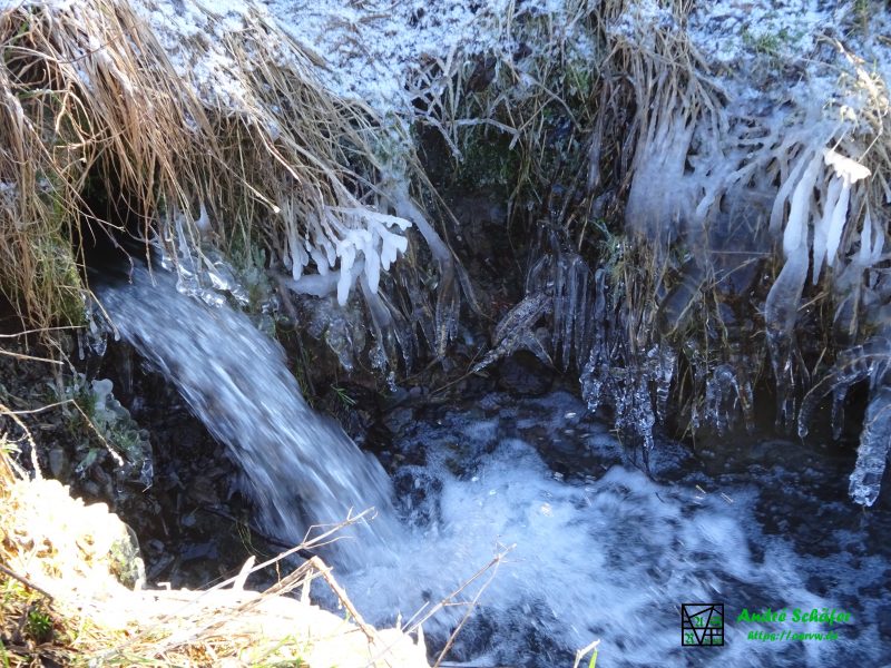 Am Auslauf des Wasser aus einem Rohr lässt Spritzwasser eine Eisschicht wachsen