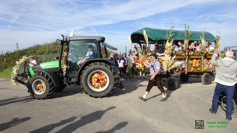 Ein Traktor mit Blumen in den Rädern und geschmücktem Anhänger biegt in die Dorfstraße ein